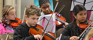 Violin students playing in the orchestra hope you'll donate so more students can join them.